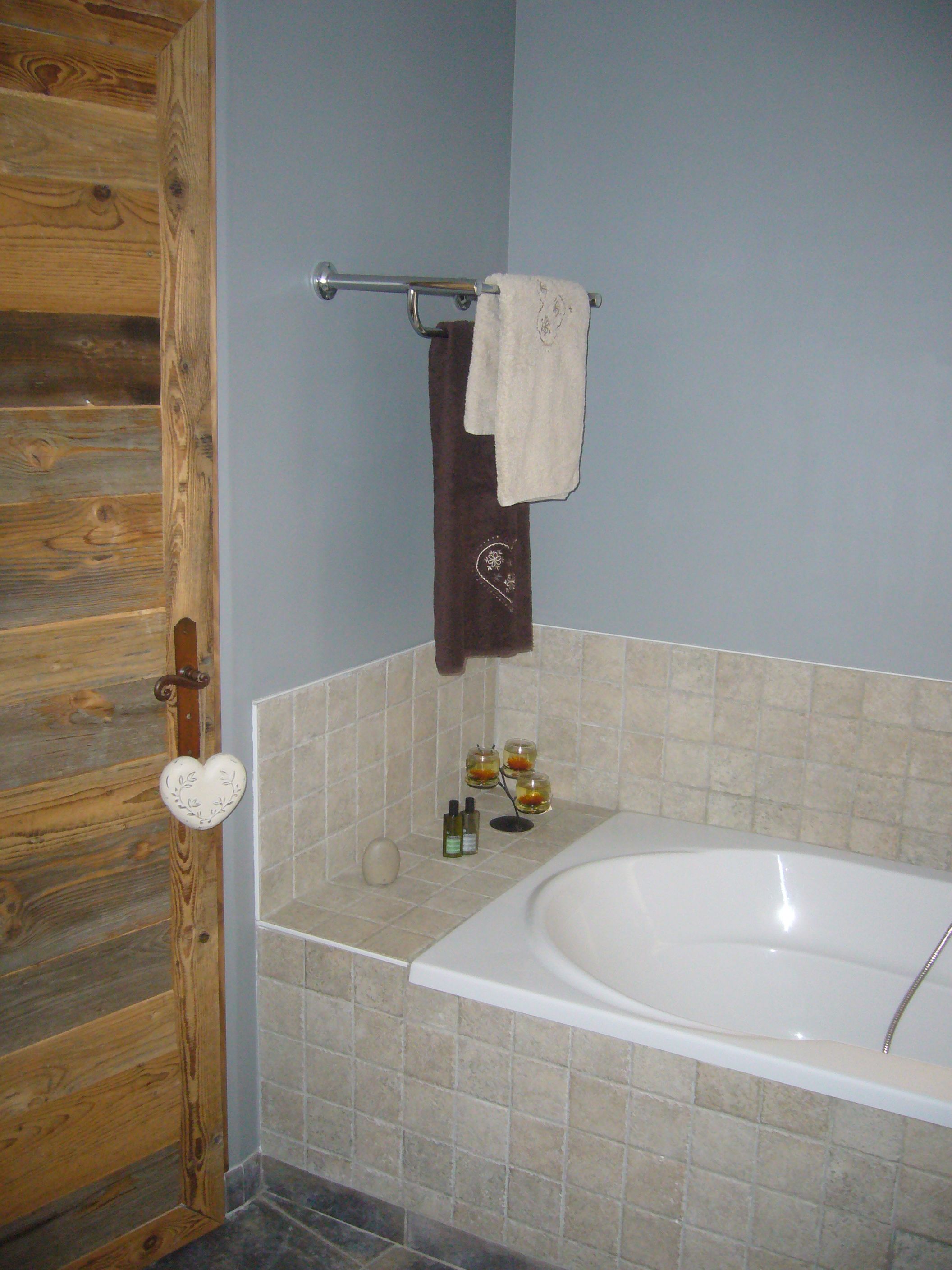 Un baño con puerta de madera, una bañera, un perchero con toalla y artículos de aseo en un estante.