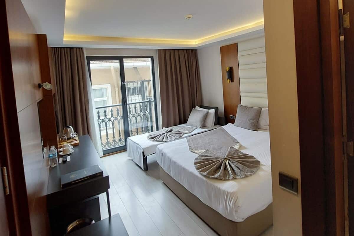 A modern hotel room with a large bed, a desk, and a balcony with a view.