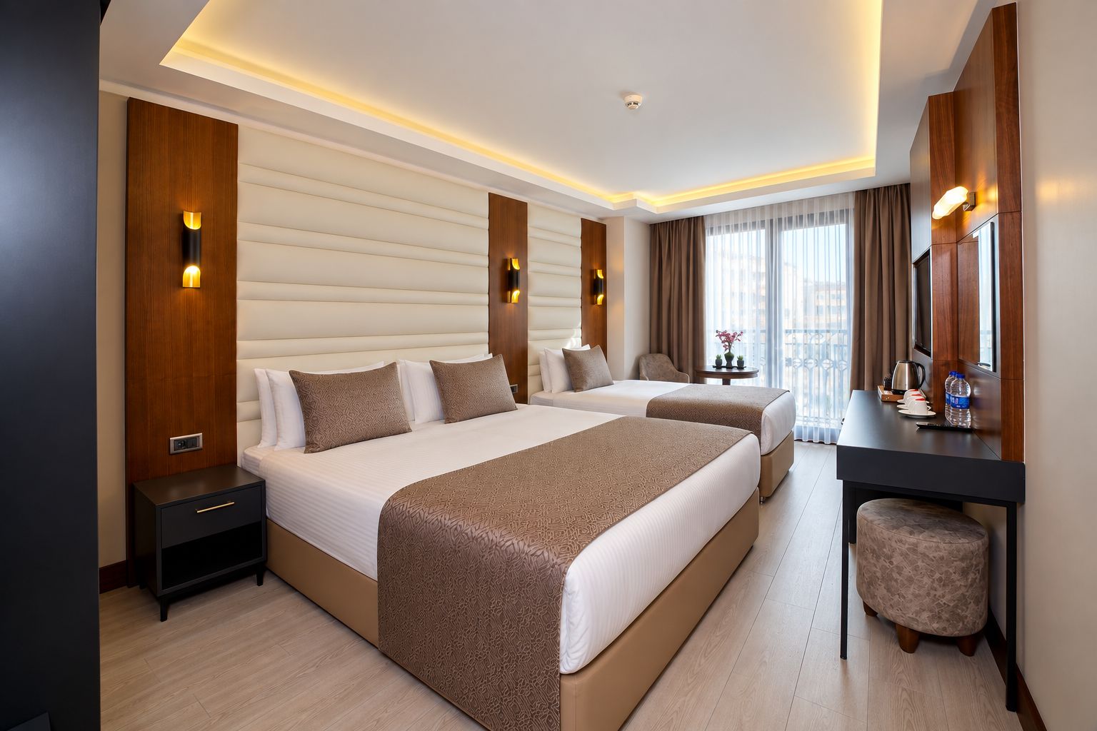 Ein Hotelzimmer mit zwei Betten, einem Schreibtisch, einem Stuhl, einem kleinen Tisch und Balkonblick.