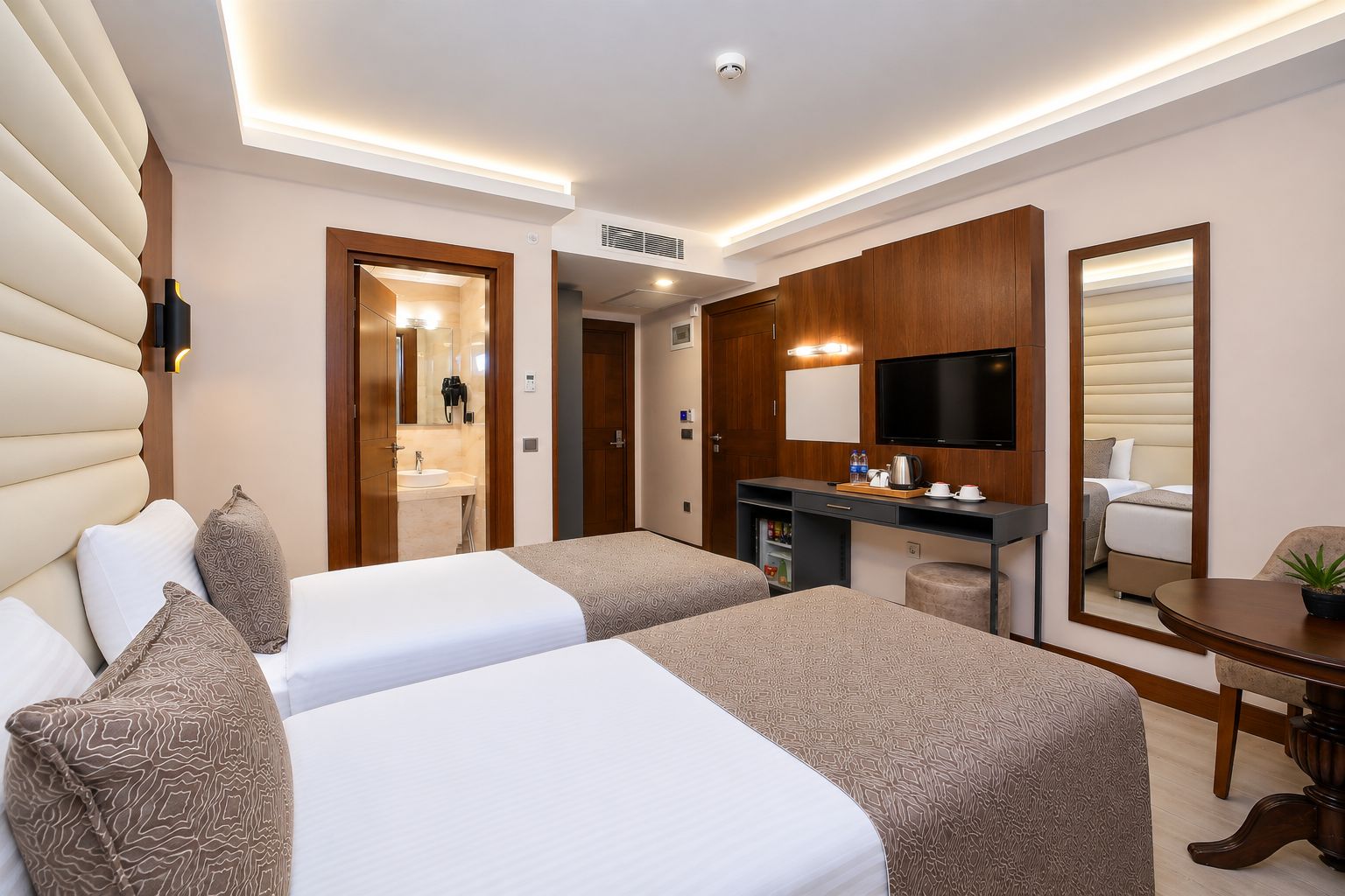 A hotel room with two beds, a desk, a television, and a bathroom visible through an open door.