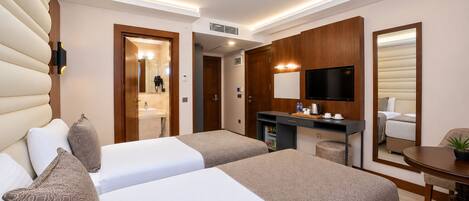 Ett hotellrum med två sängar, ett skrivbord, en tv och ett badrum som syns genom en öppen dörr.