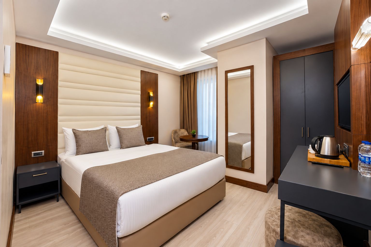A modern hotel room with a large bed, bedside tables, a desk with a kettle, and a mirror.