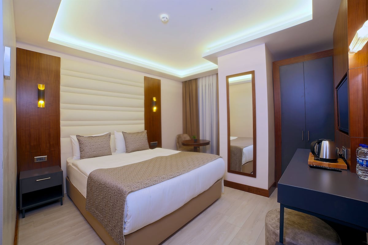 A hotel room with a large bed, bedside tables, a desk with a kettle, and a mirror.