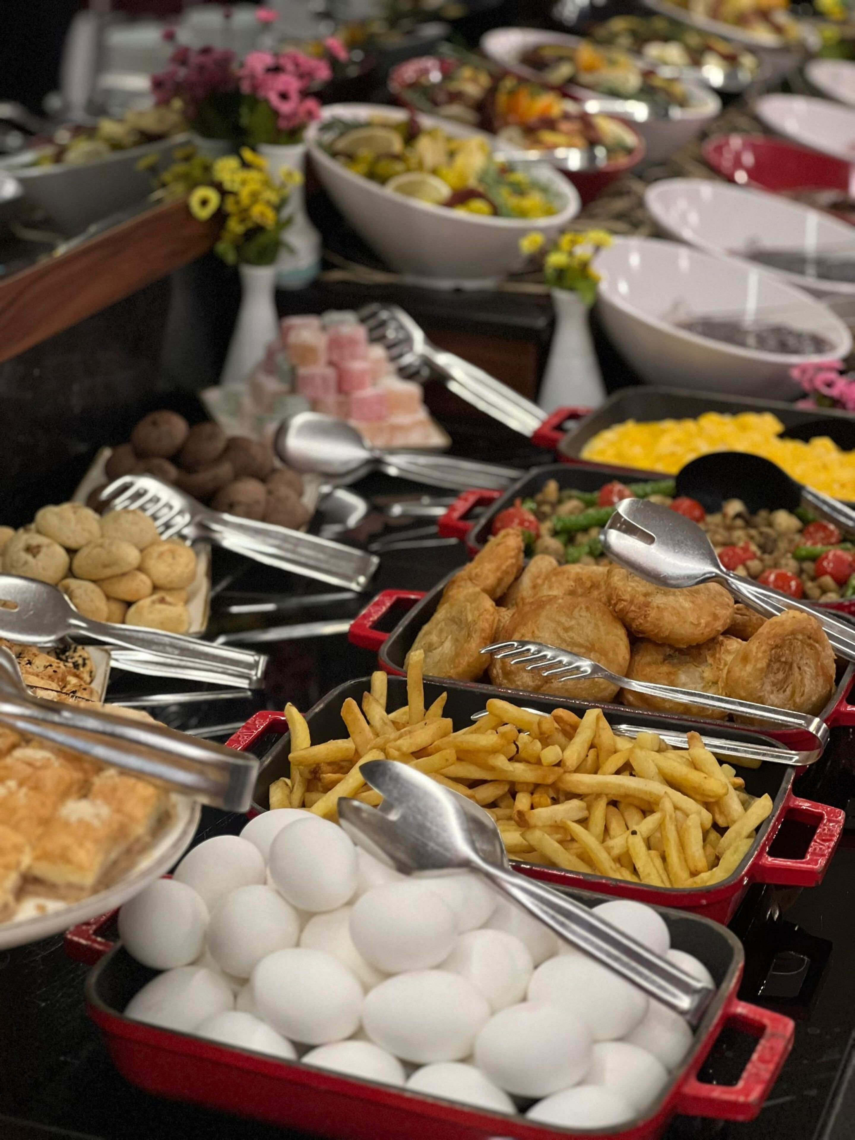 Un bufé con diversos alimentos, incluyendo huevos, papas fritas y diferentes tipos de carne.