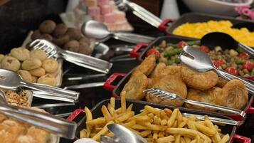 Un bufé con diversos alimentos, incluyendo huevos, papas fritas y diferentes tipos de carne.