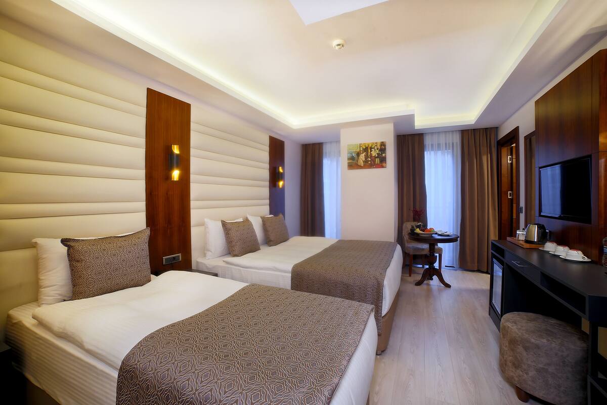 A hotel room with two beds, a desk, a TV, and a dining table.