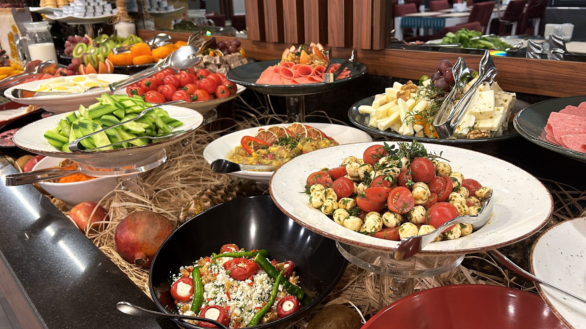 Een buffet met diverse gerechten, waaronder salades, fruit en vlees.