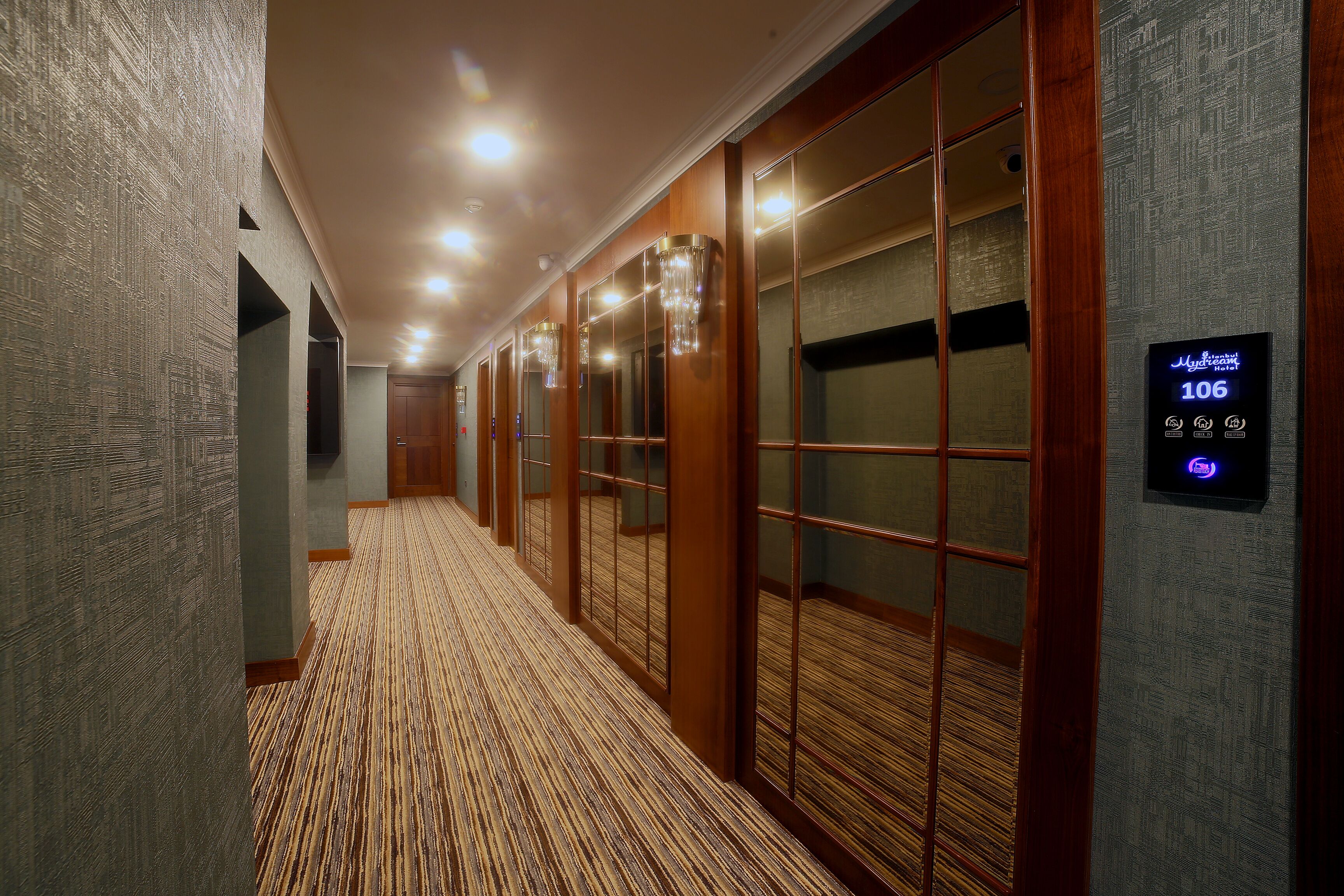 A hallway with wooden paneling, a patterned carpet, and a digital display showing room number 106.