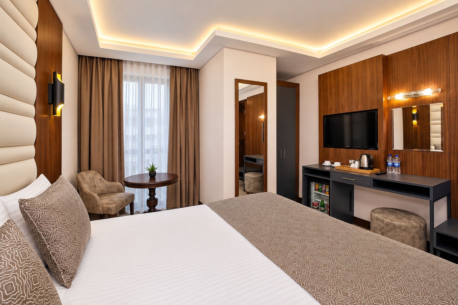 A hotel room with a large bed, a desk with a flat-screen TV, a small table with a plant, and a wardrobe.