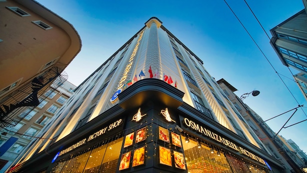 Un edificio alto con un letrero llamativo que indica 'OSMANLIZADELER FACTORY SHOP' en su base.