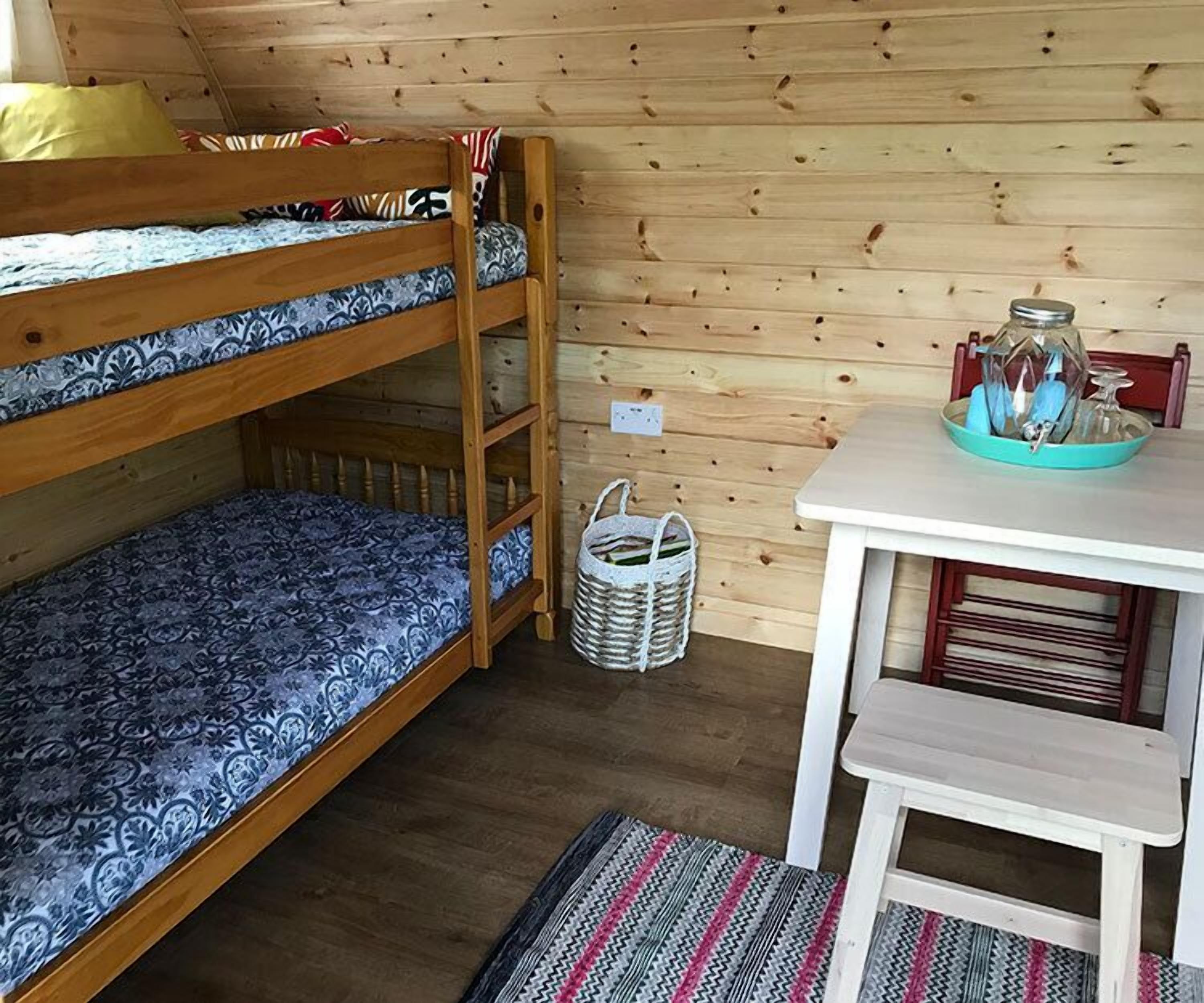 A bunk bed with patterned bedding, a small table with a tray, and a woven basket.