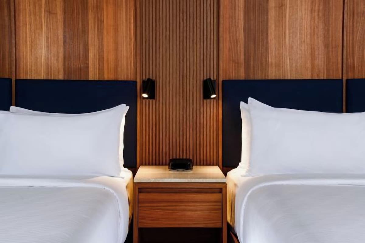A hotel room with two beds, wooden paneling on the walls, and bedside lamps.