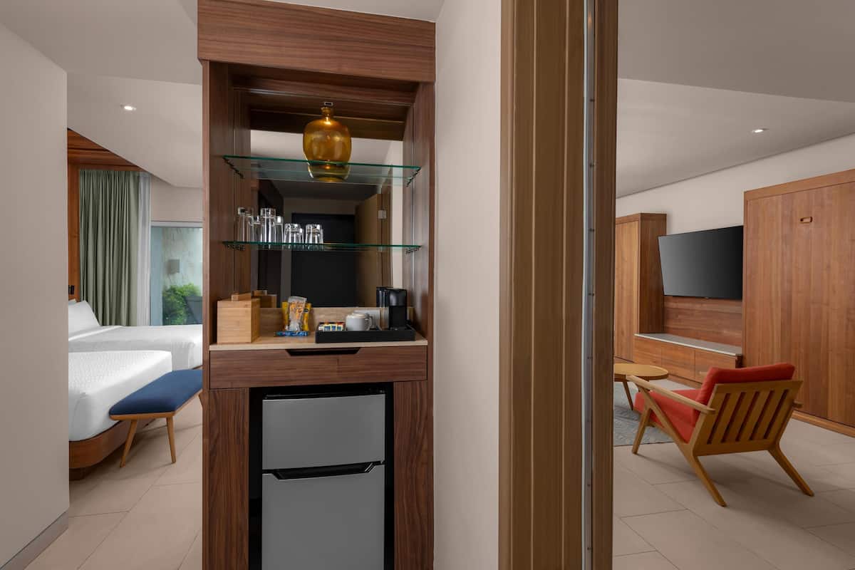 A compact hotel room with a kitchenette, a bed with a blue bench, a small dining table, and a TV.
