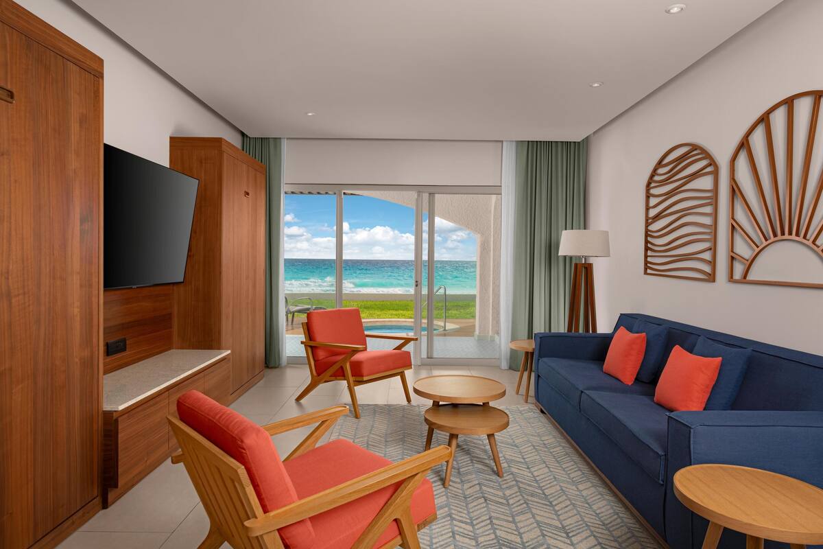 A modern hotel room with a large TV, wooden furniture, a blue sofa, and a view of the ocean.