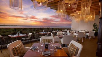An outdoor dining area with tables and chairs, overlooking a scenic sunset view.