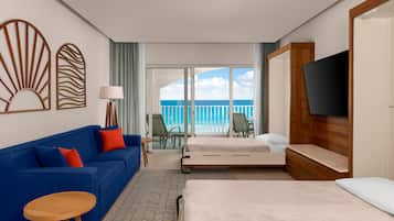 Quarto de hotel com cama, sofá azul, televisão e varanda vista para o oceano.