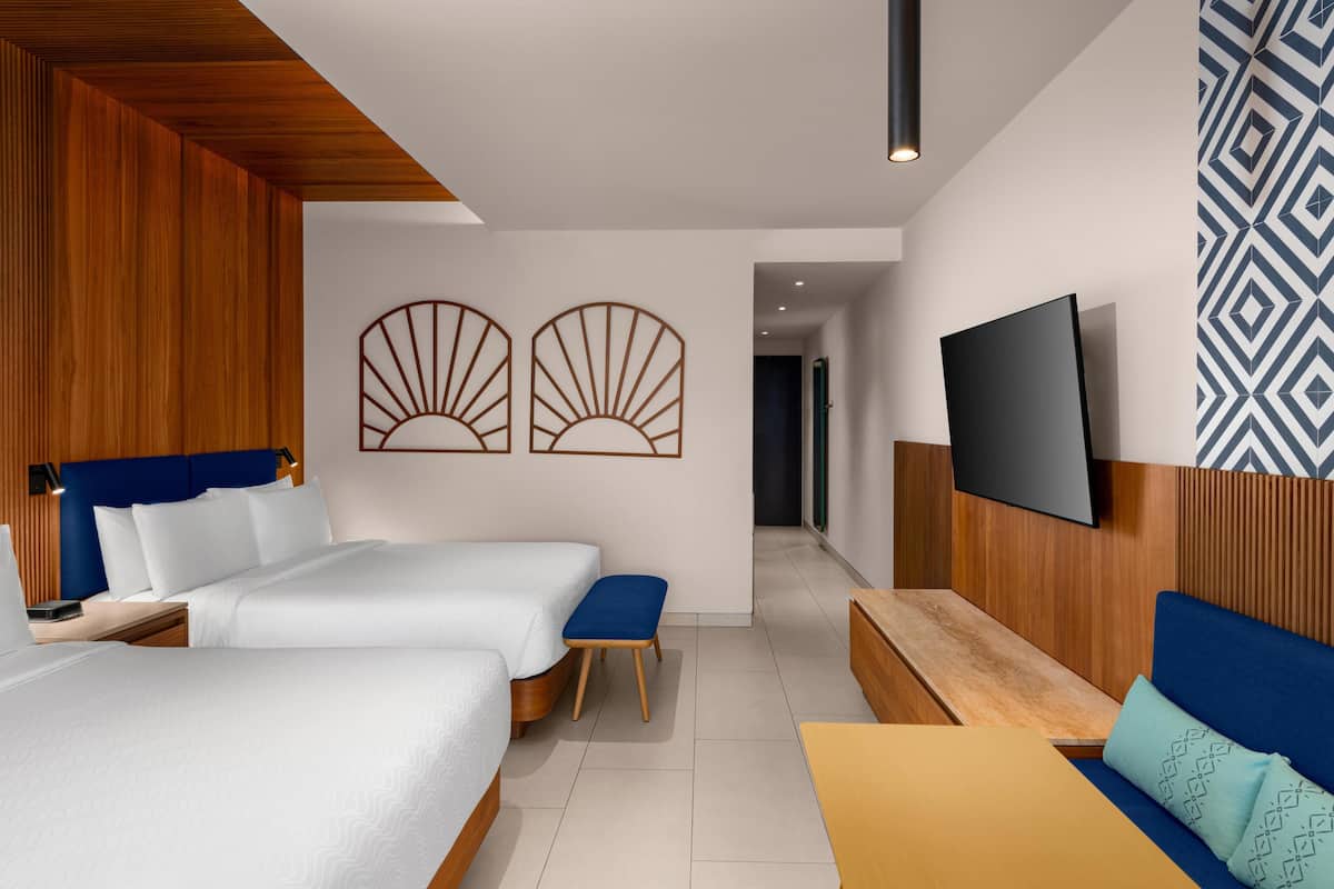A modern hotel room with two beds, a sofa, a TV, and decorative wall art.