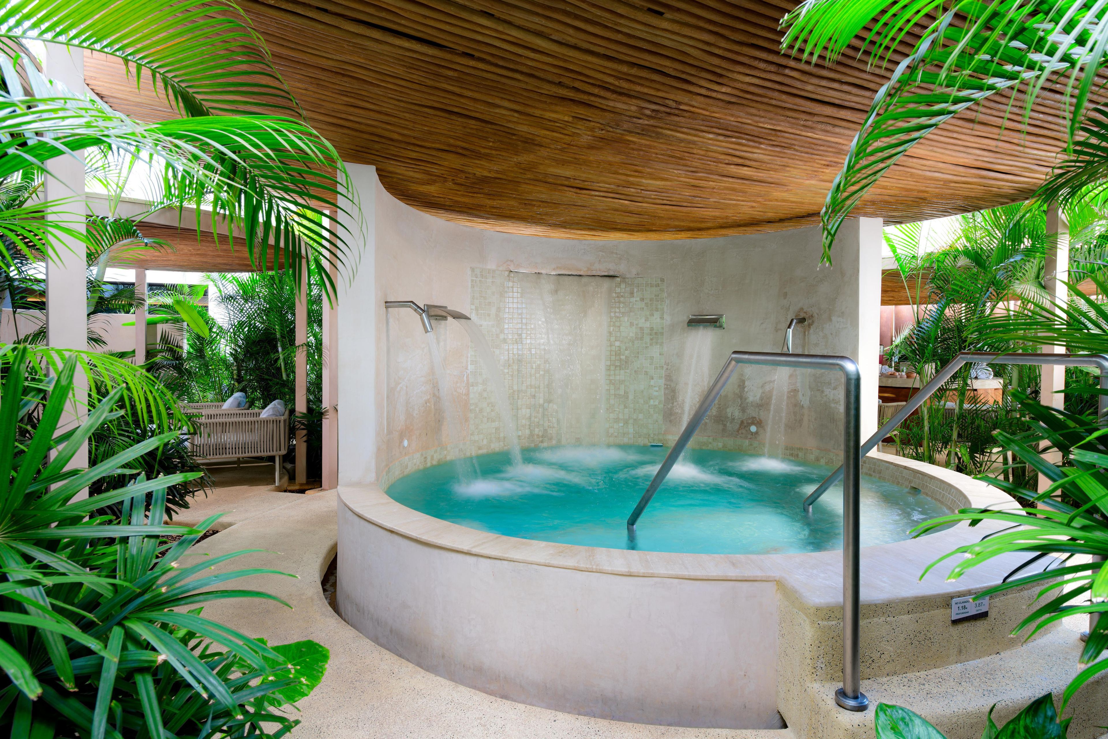 A hot tub with a tiled wall and a wooden ceiling, surrounded by lush greenery.