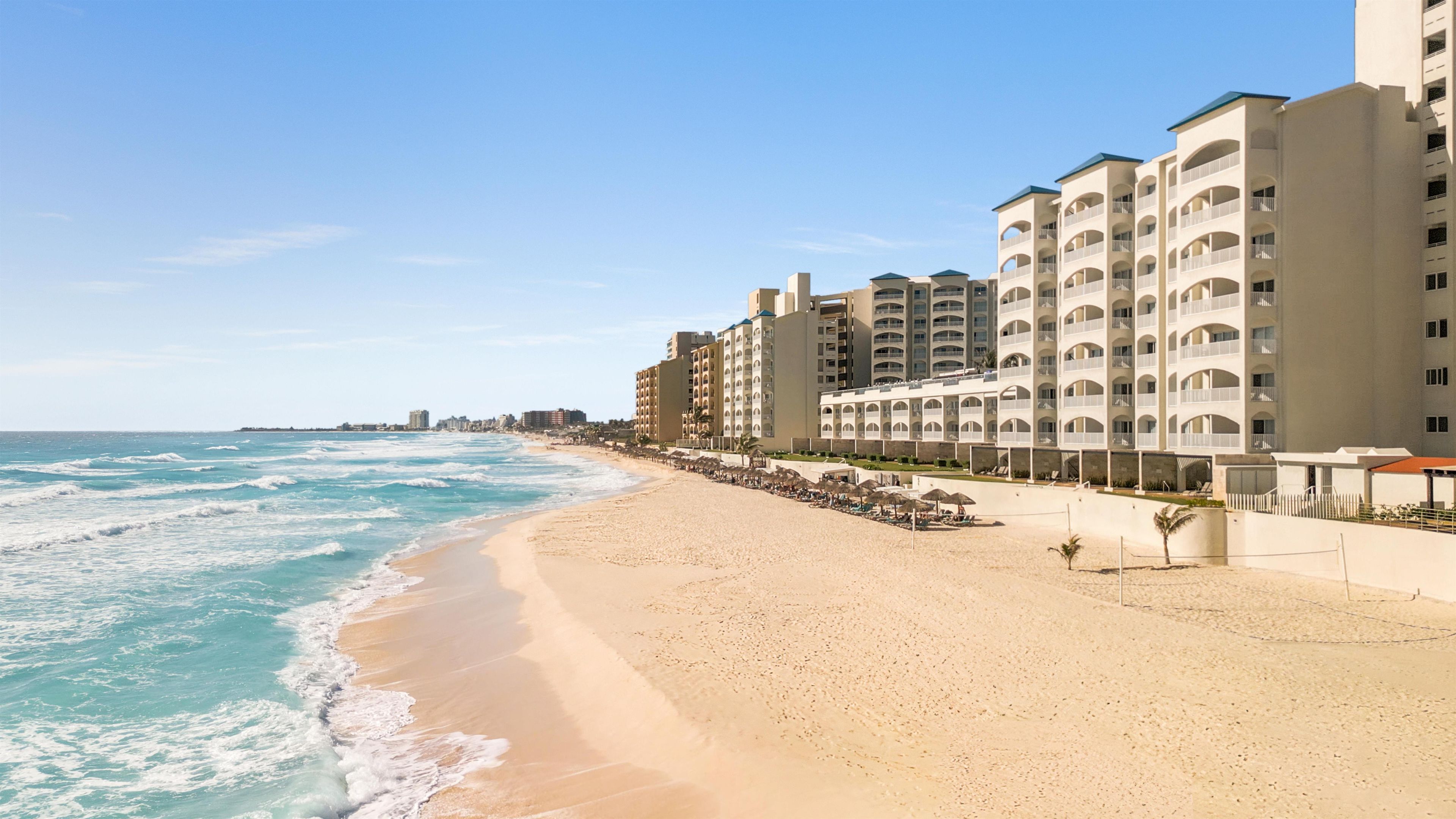 A beachfront hotel with multiple balconies, a sandy beach, and ocean waves.