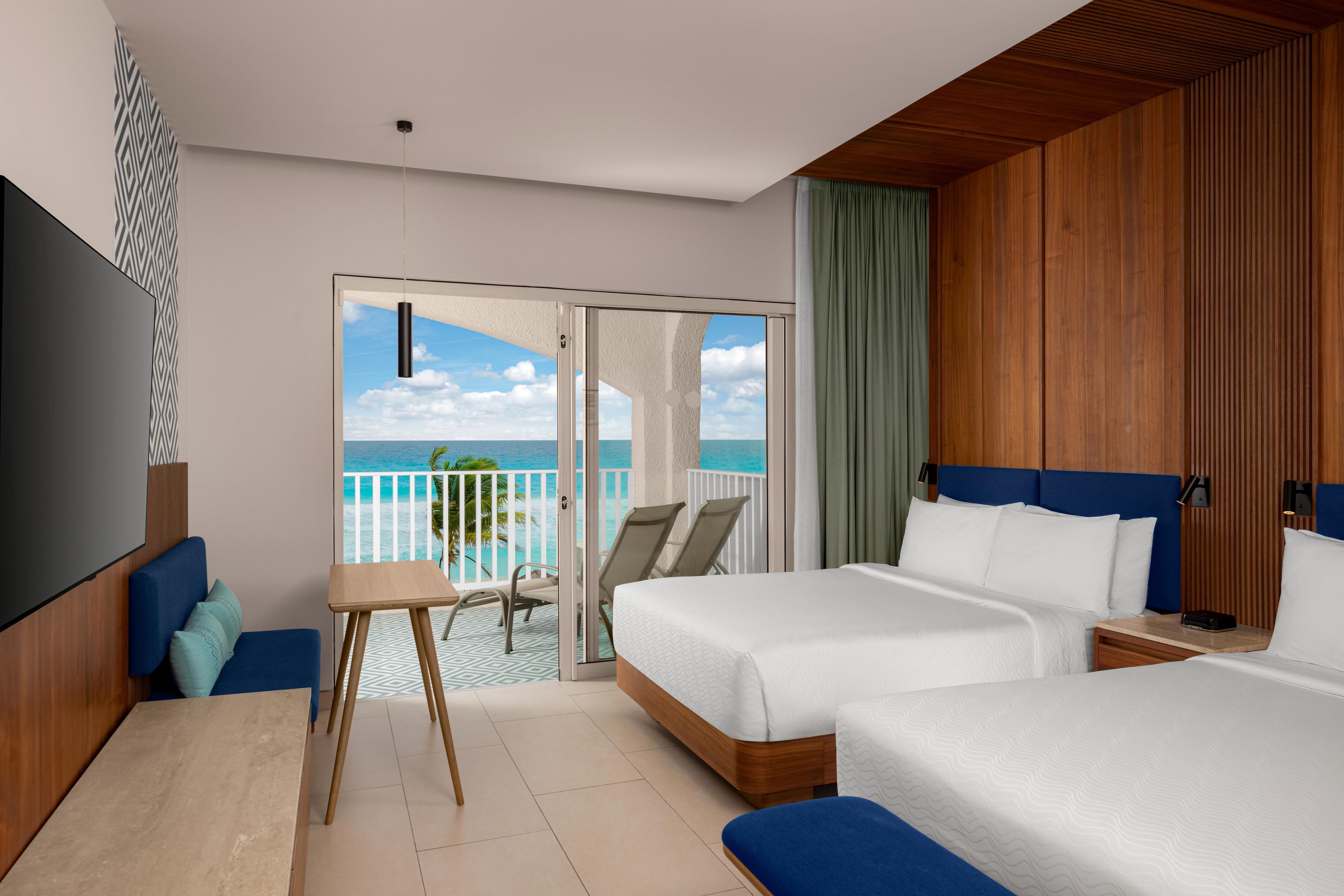Habitación de hotel con balcón, dos camas, televisor y una mesita.