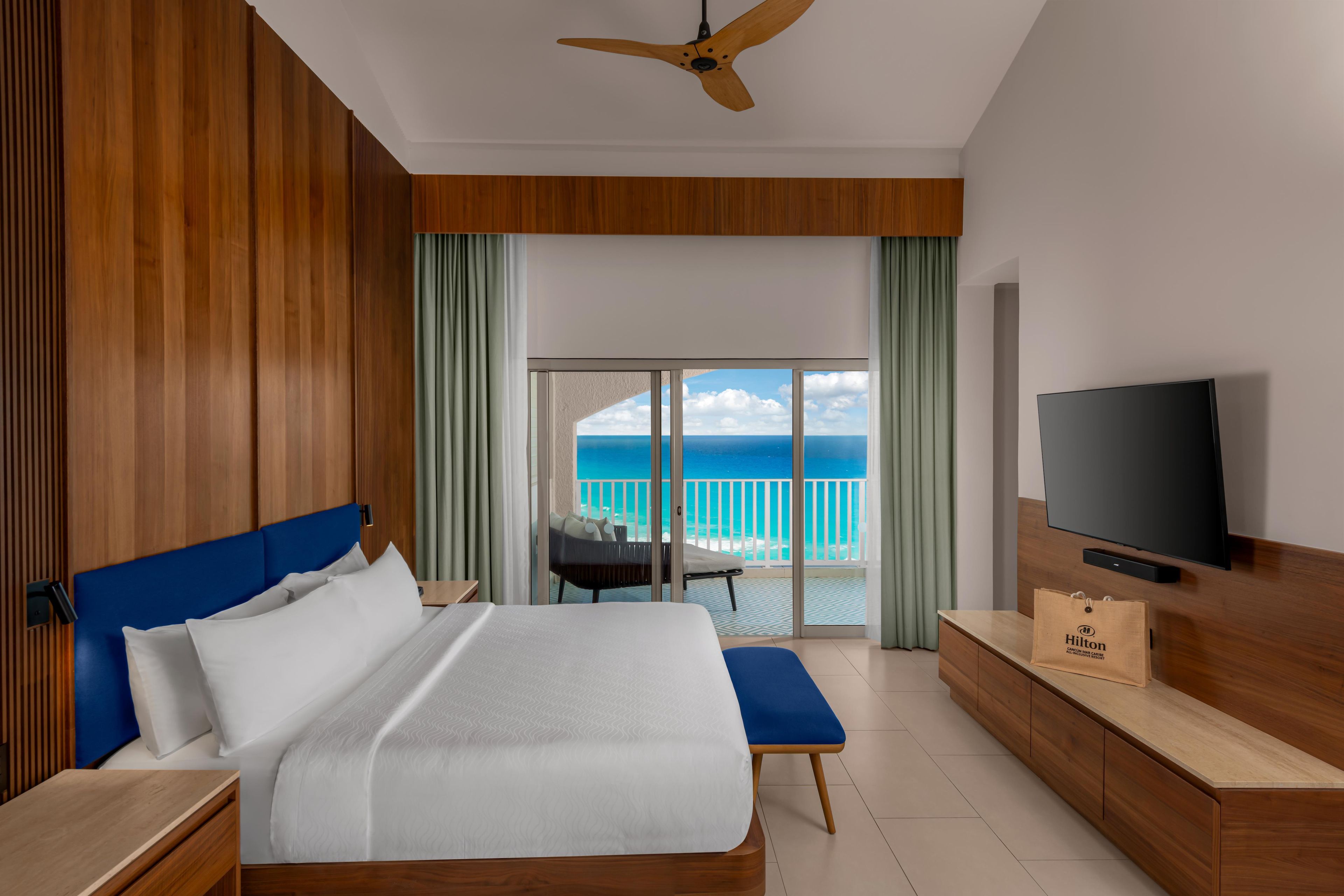Habitación de hotel con cama, televisión, minibar y balcón con vista al océano.