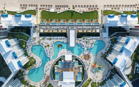 An aerial view of a resort with multiple swimming pools, a beach, and a central building.