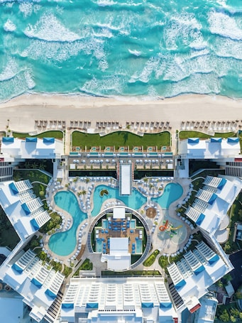 An aerial view of a resort with multiple swimming pools, a beach, and a central building.
