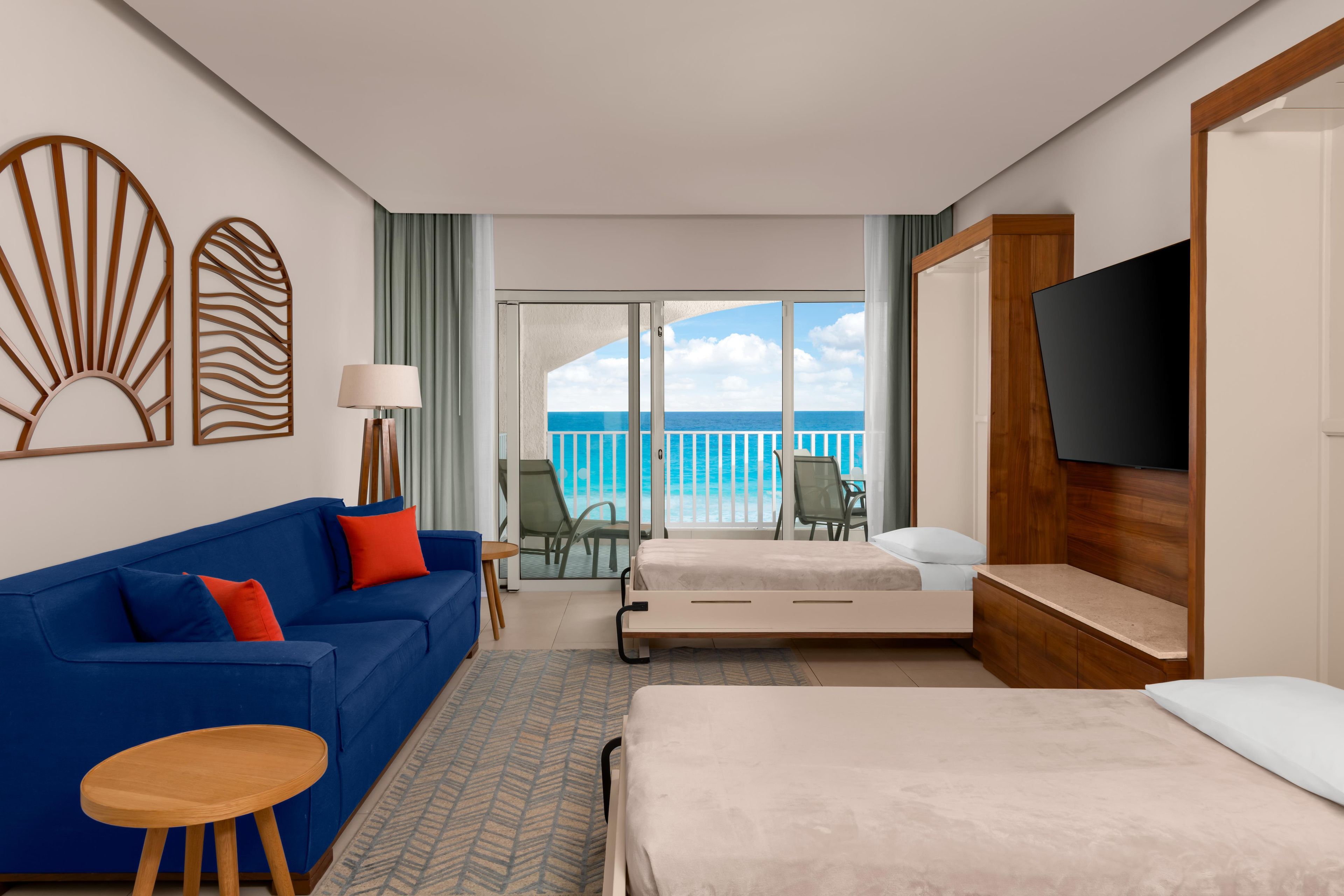 Une chambre d’hôtel avec un lit, un canapé bleu, une petite table, une télévision et un balcon donnant sur l’océan.