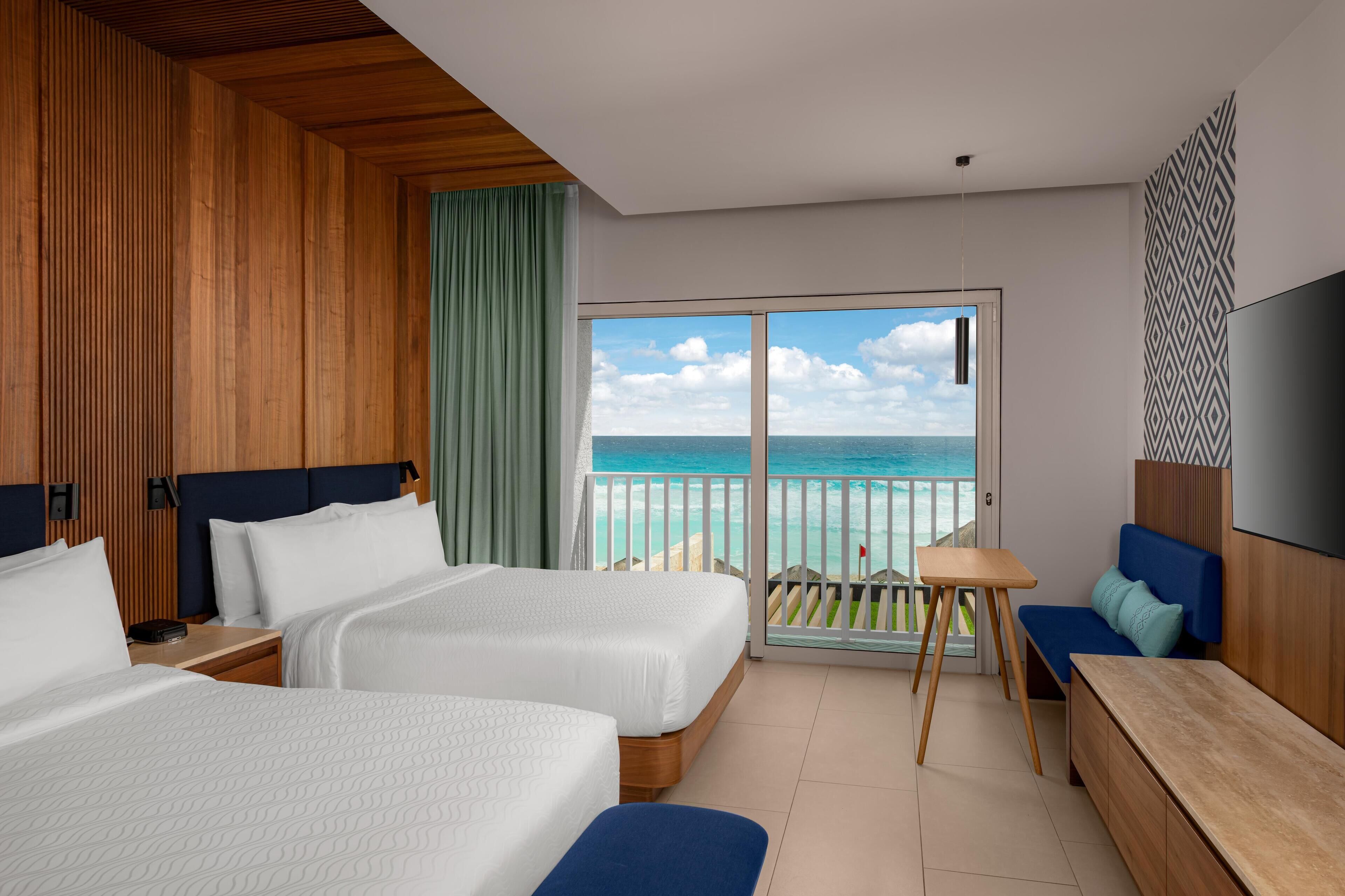 A hotel room with two beds, a TV, a balcony with a view of the sea, and a wooden ceiling.