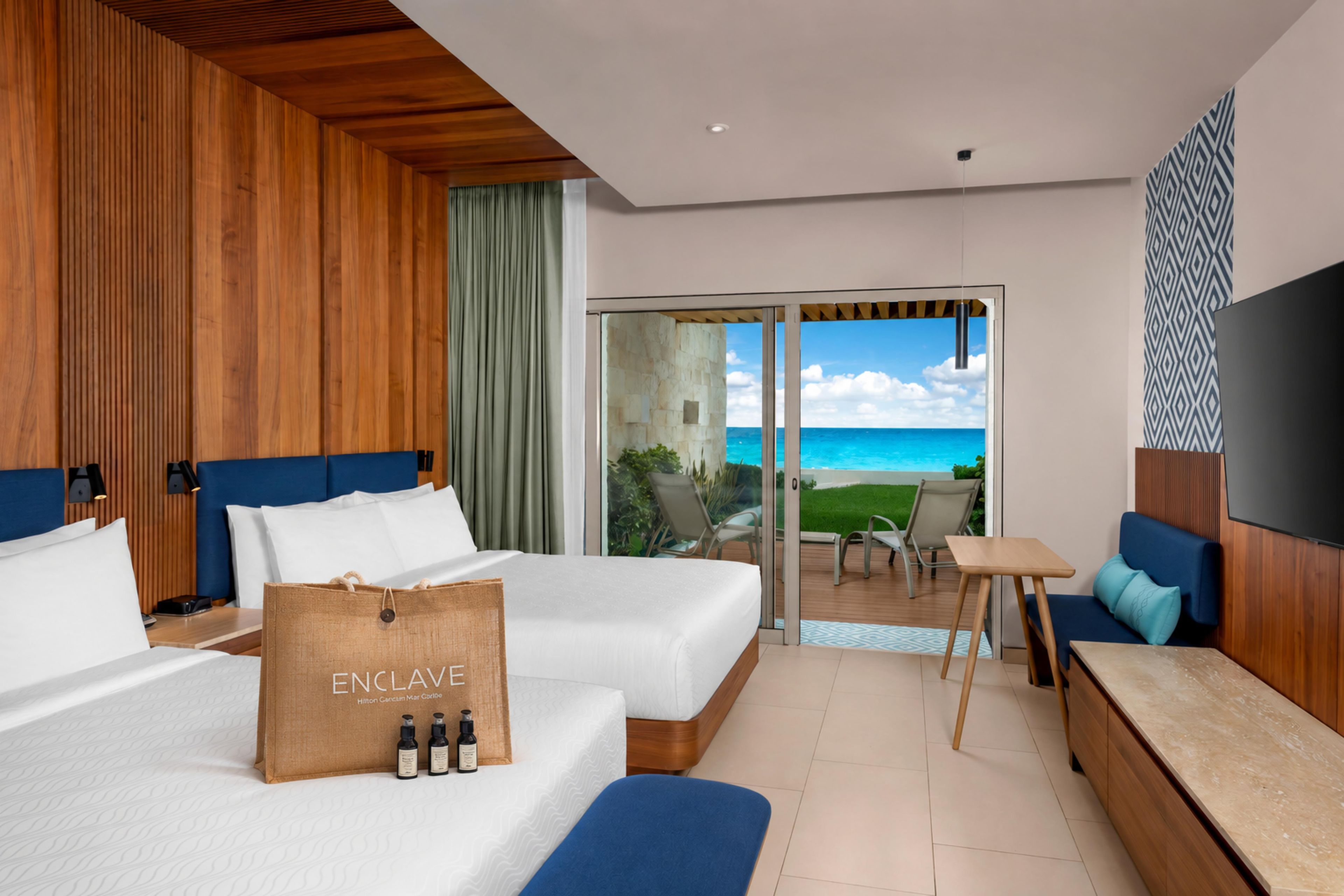A hotel room with two beds, a sofa, a small table, and a balcony with a view of the ocean.