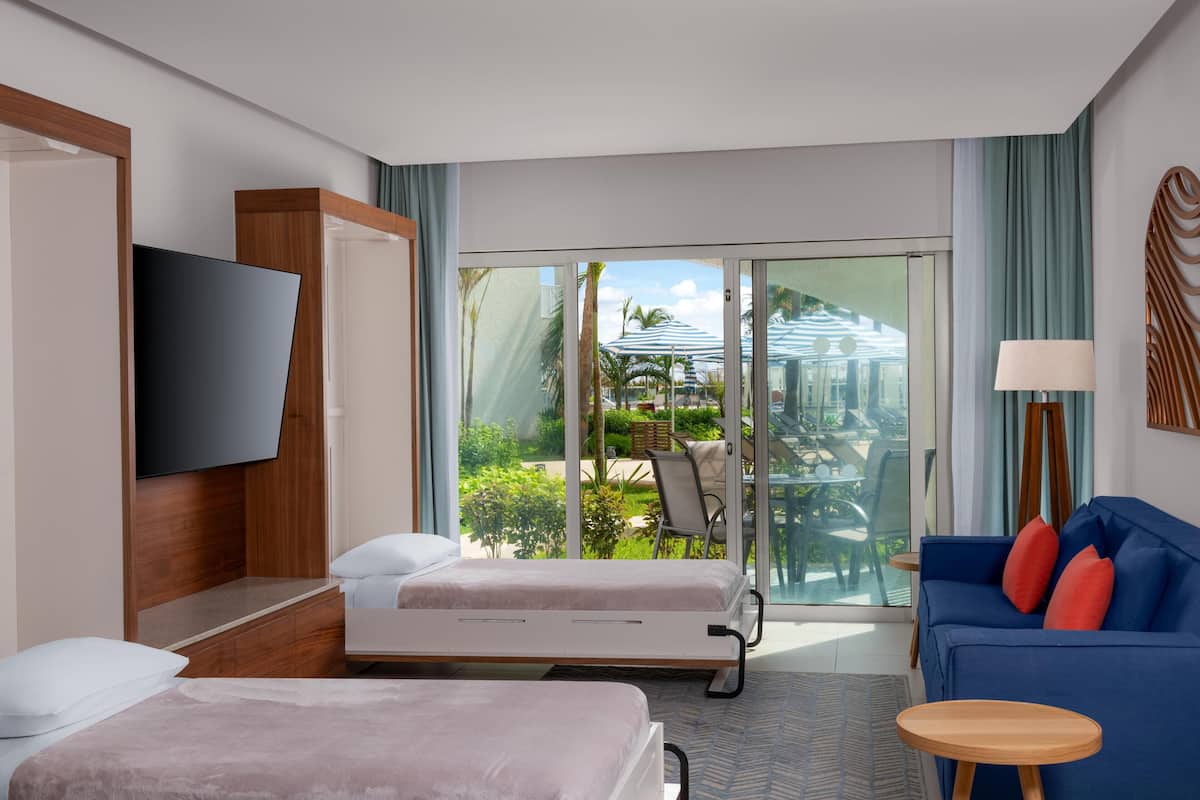 A hotel room with a bed, a sofa, a TV, and a view of the outdoors.