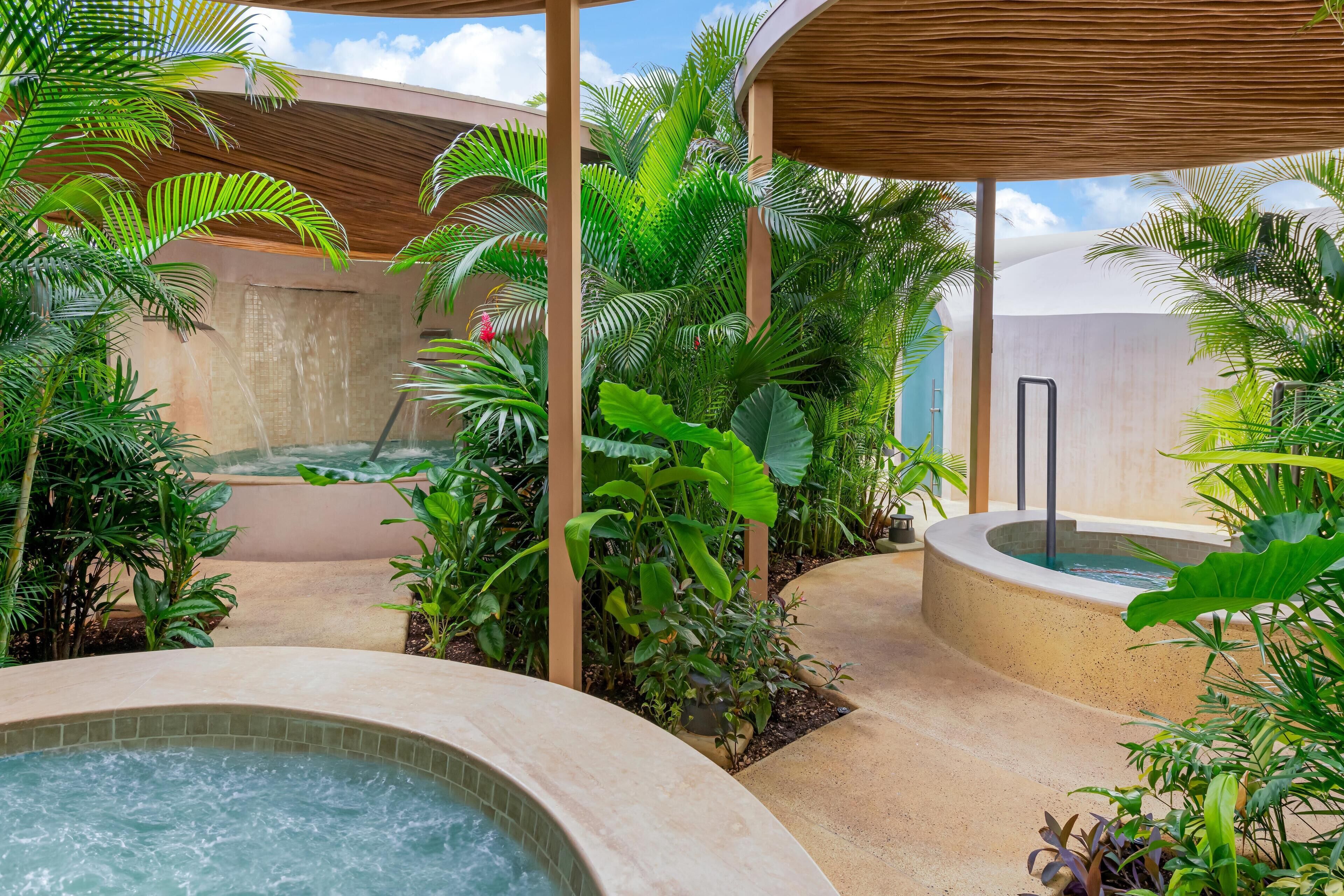 Un espace de détente avec un jacuzzi, entouré d’une végétation tropicale luxuriante et agrémenté d’une pergola en bois.