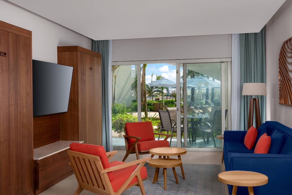 A modern hotel room with a TV, wooden furniture, a blue sofa, and a view of the outdoor area.