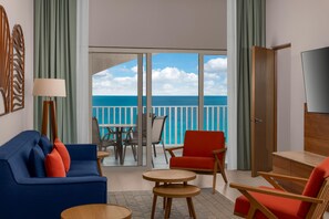 A hotel room with a balcony, a blue sofa, a red armchair, a wooden coffee table, and a TV on the wall. - Hilton Cancun Mar Caribe All-Inclusive Resort (Cancun)