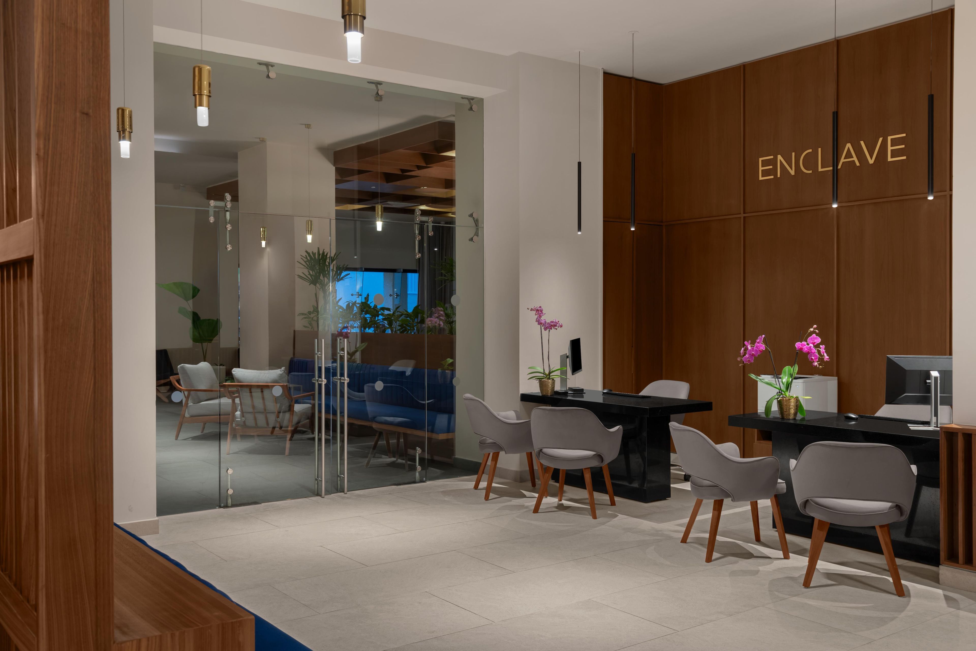 A modern reception area with a glass partition, wooden paneling, and a reception desk with chairs.