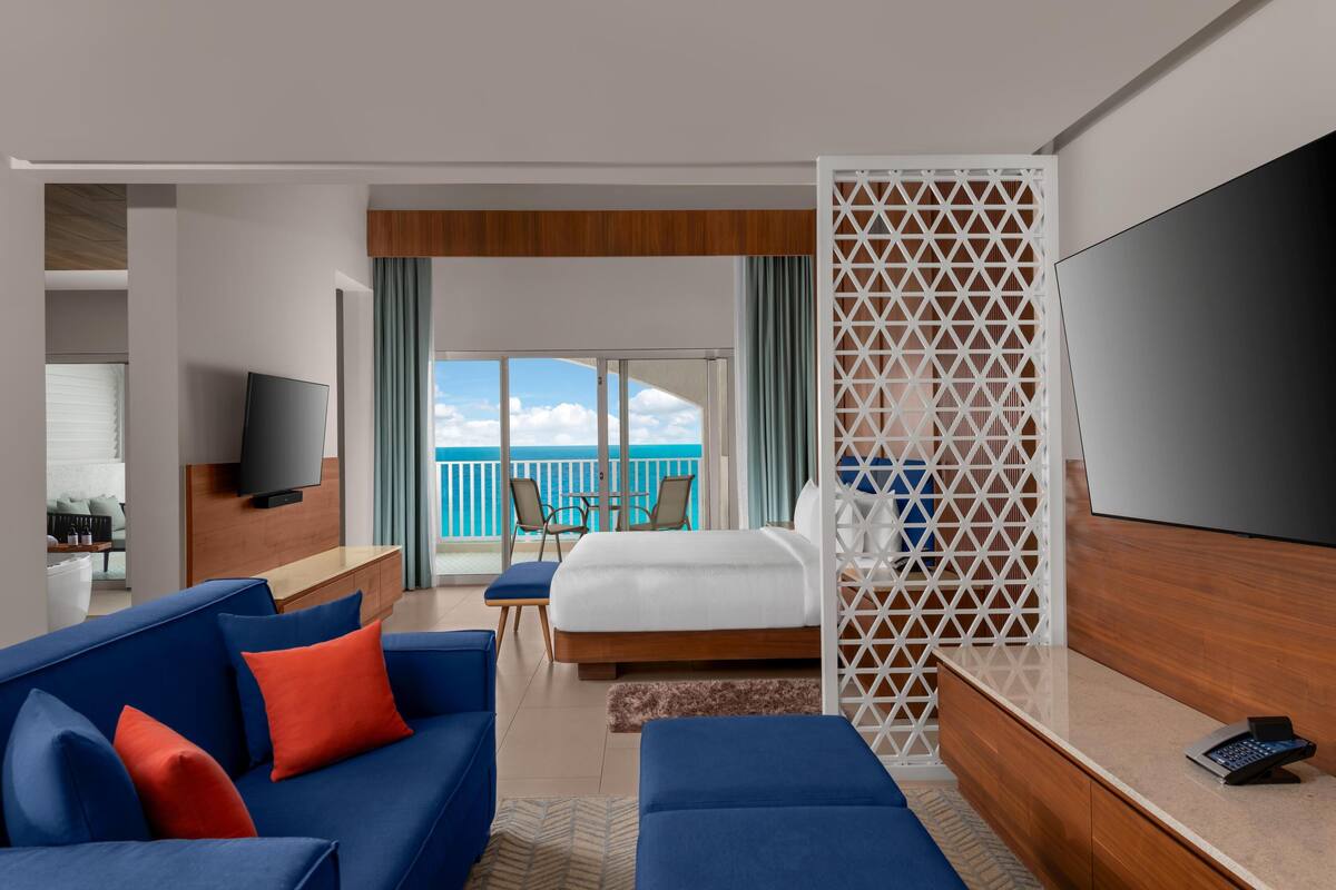 A hotel room with a bed, a TV, a sofa, and a balcony with a view.