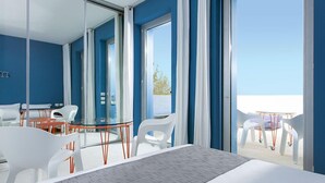A modern hotel room with a large bed, a glass table, white chairs, and a balcony with outdoor seating. - Calcebianca (Ostuni)