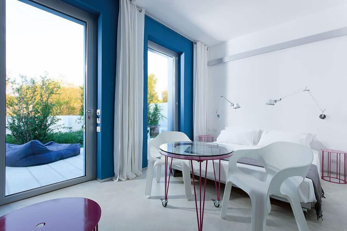 Ein modernes Zimmer mit einem Glastisch, weißen Stühlen, einem weißen Sofa und einer Glastür, die zu einem Außenbereich führt.