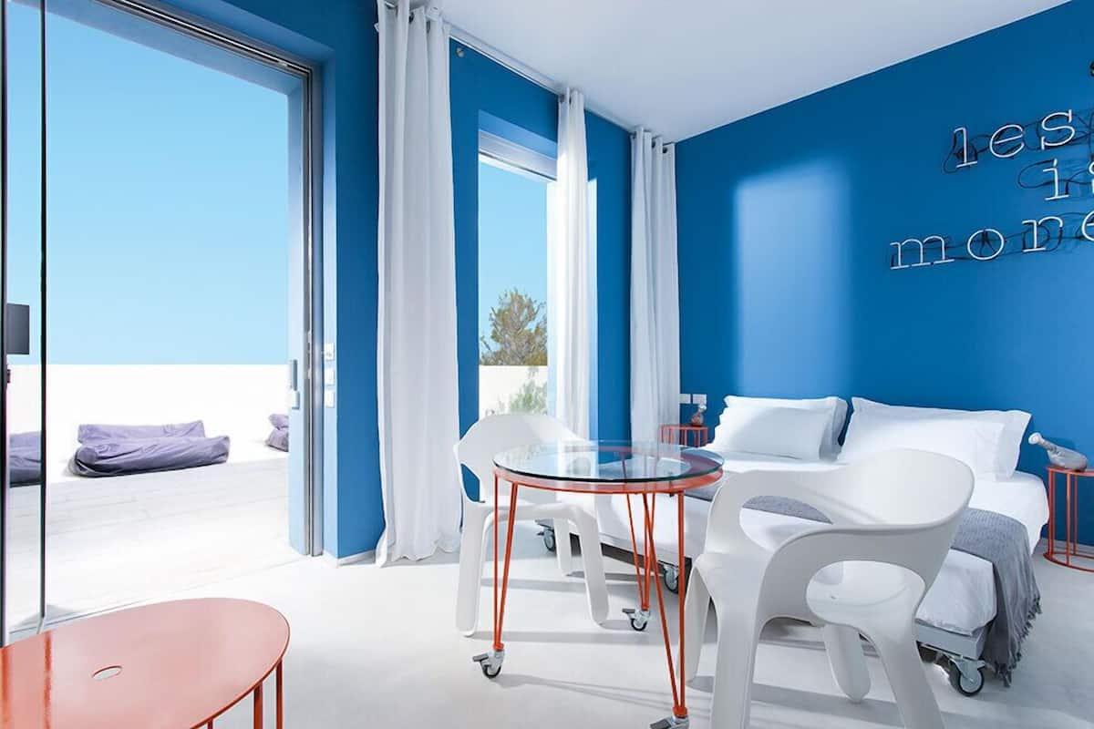 Ein modernes Zimmer mit blauer Wand, weißen Möbeln und einem Glastisch.