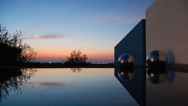 A serene evening view of a modern building with a reflective pool, capturing the sunset and city lights in the background. - Calcebianca (Ostuni)