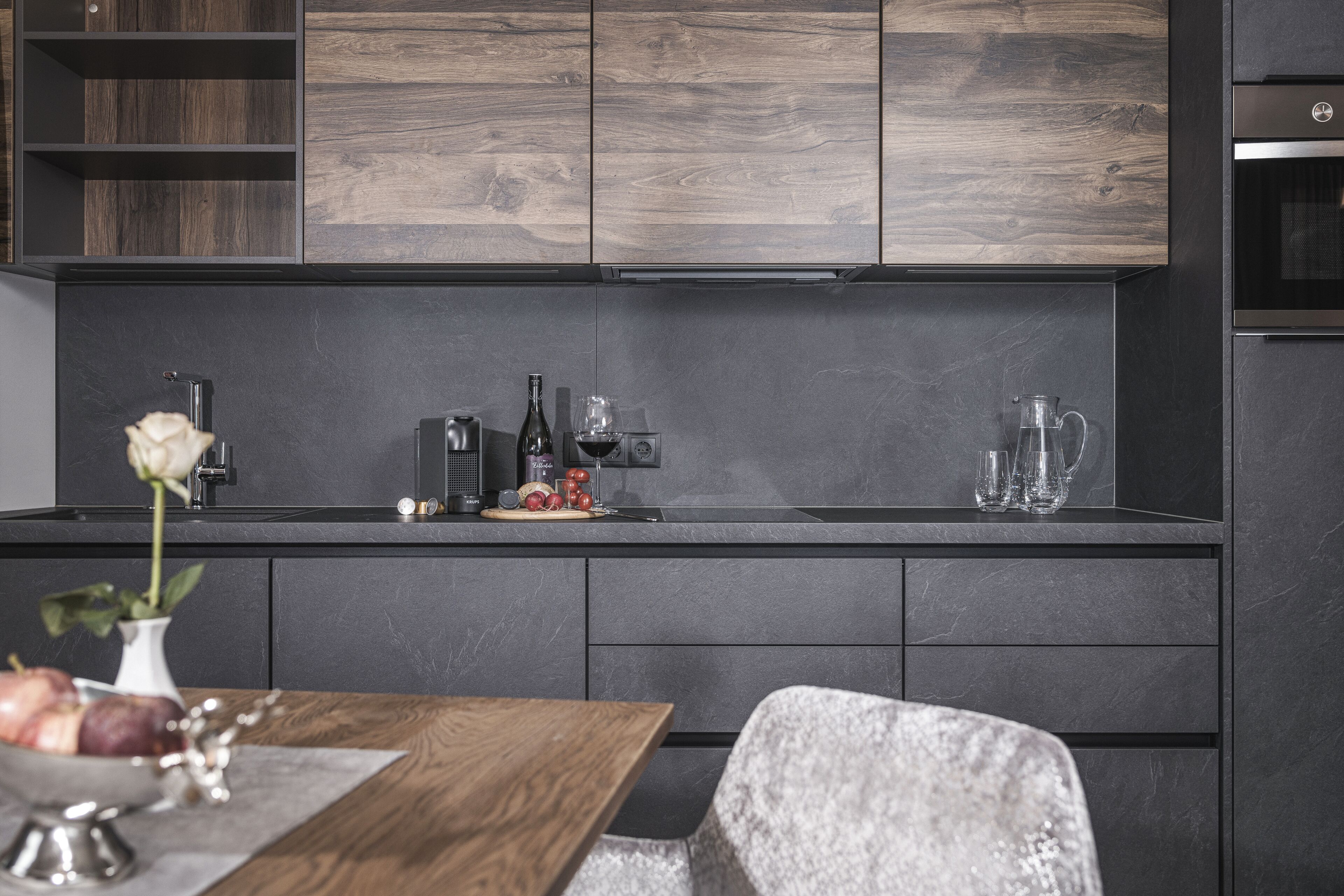 A modern kitchen with dark cabinetry, a wooden countertop, and a dining area with a table and chairs.