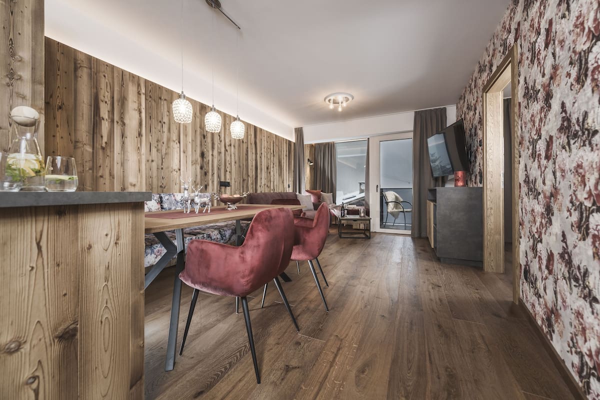 Une cuisine moderne avec des murs en bois, un coin repas avec une table en bois et des chaises rouges, et un téléviseur fixé au mur.