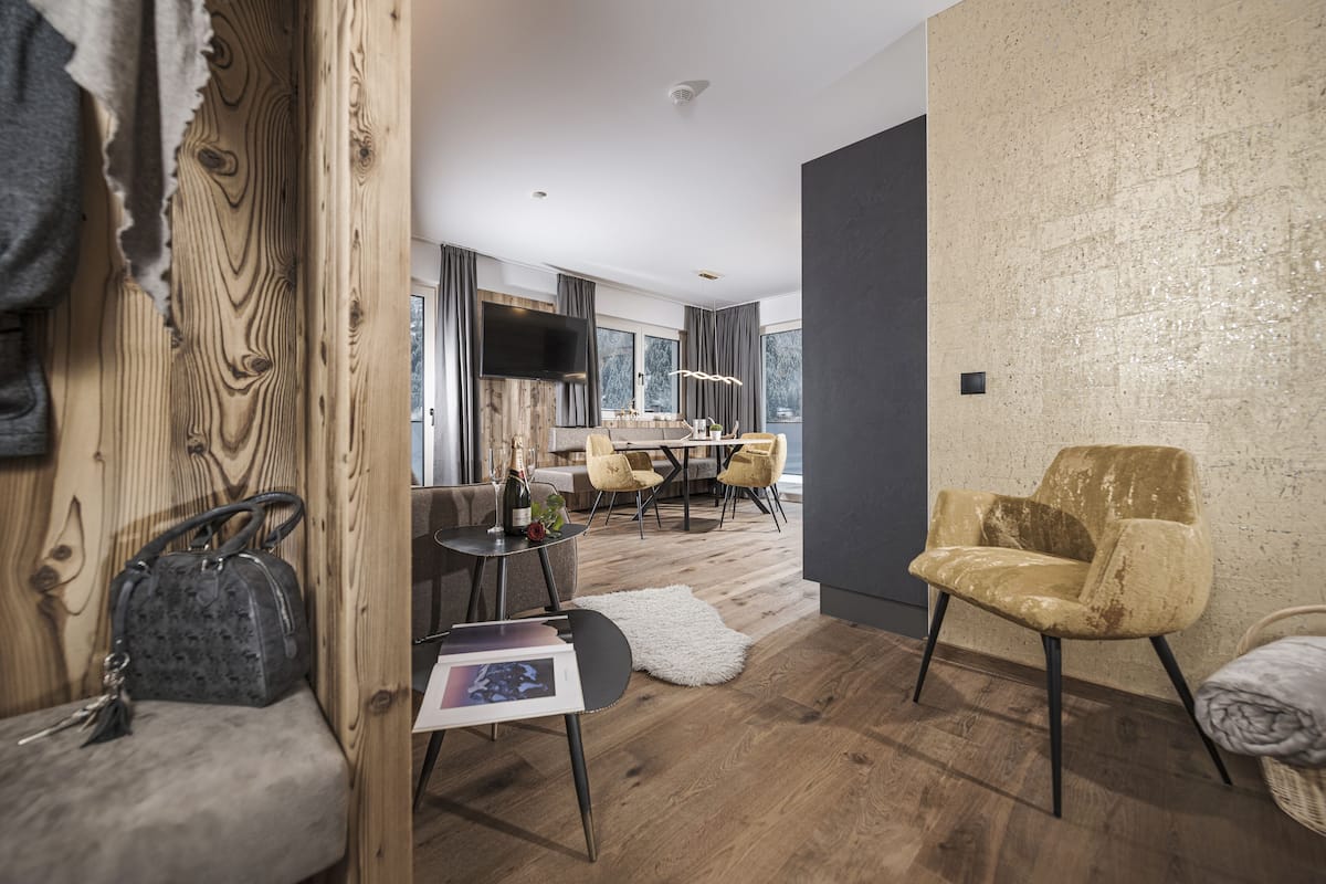Un salon moderne avec un mur d’accent en bois, un canapé, un fauteuil, un coin repas avec une table et des chaises, et une grande fenêtre offrant une vue.