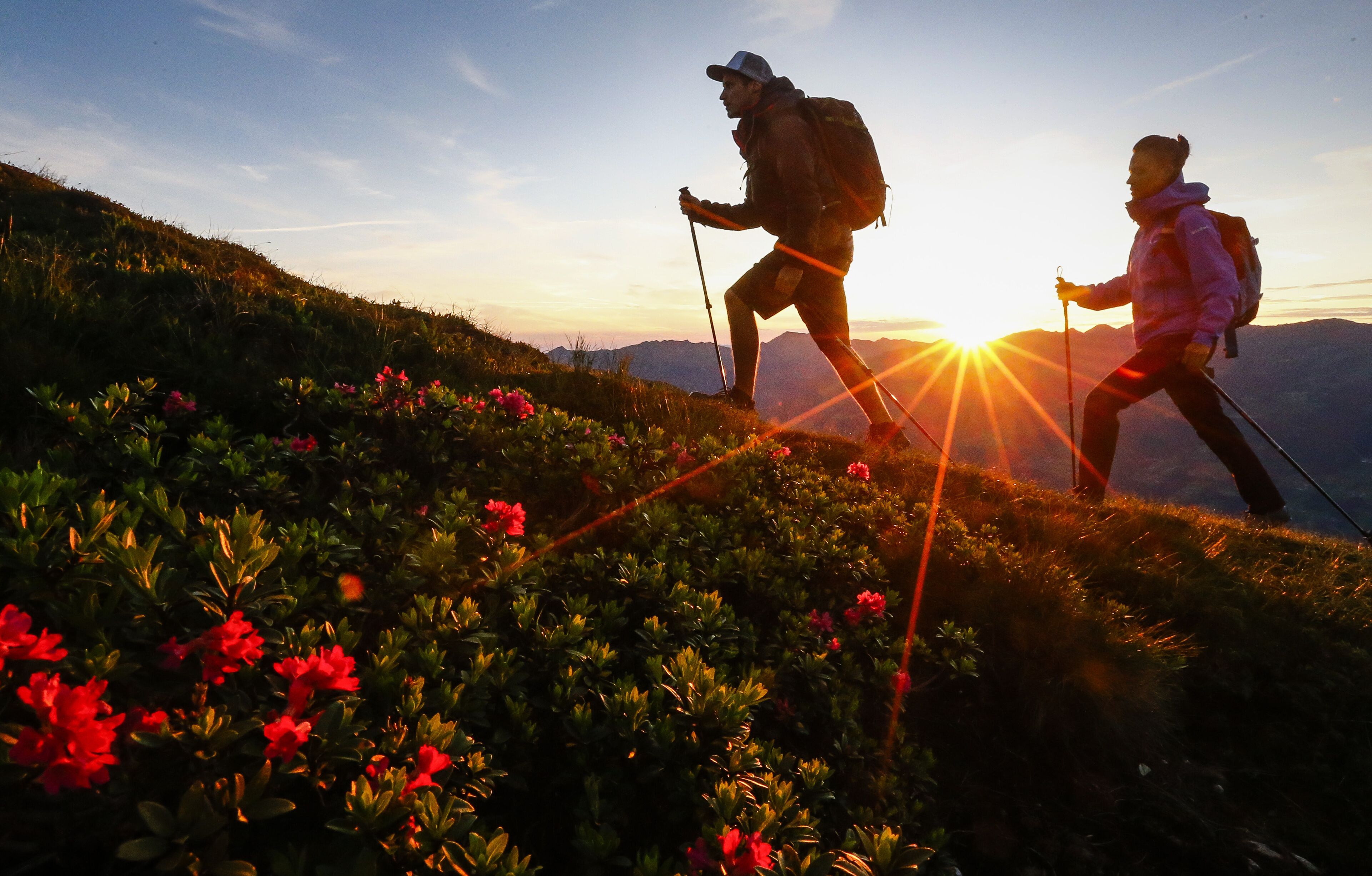 Dos excursionistas en una colina cubierta de hierba con el atardecer al fondo.