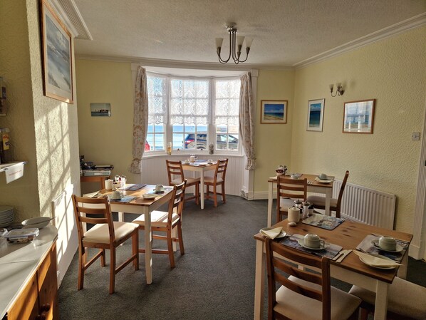 A dining area with wooden tables and chairs, a chandelier, and a view of the sea through large windows.