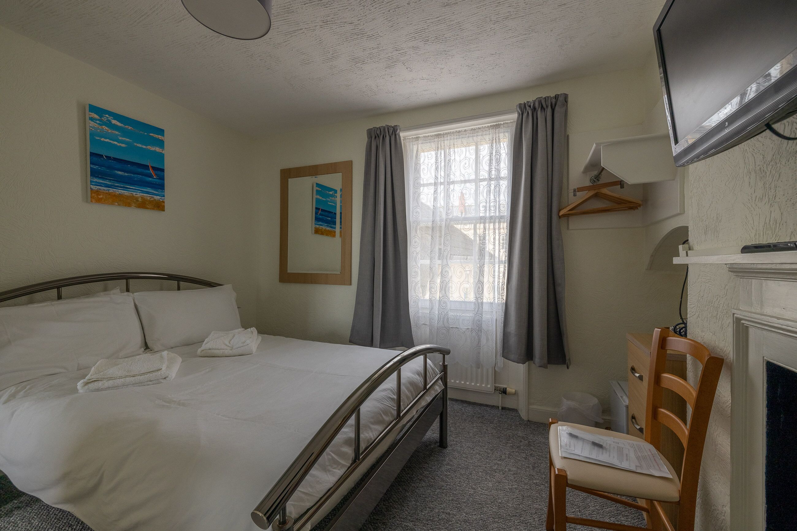 Una camera d'albergo con un letto, una sedia, una televisione, un caminetto e una finestra con tende.