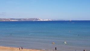 A beach with clear blue water, a sandy shore, and distant cliffs. - The Seaspray (Weymouth)