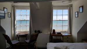 A hotel room with a bed, two chairs, a desk, and a view of the sea through large windows. - The Seaspray (Weymouth)