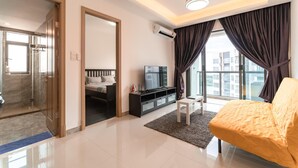 A modern living room with a sofa, a TV, and a glass door leading to a bathroom. - R&F Princess Cove at R&F Mall (Johor Bahru)