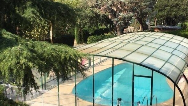 En swimmingpool med et glasmur, omgivet af træer og et hegn.